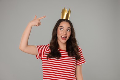 Photo of Beautiful young woman pointing at princess crown on grey background
