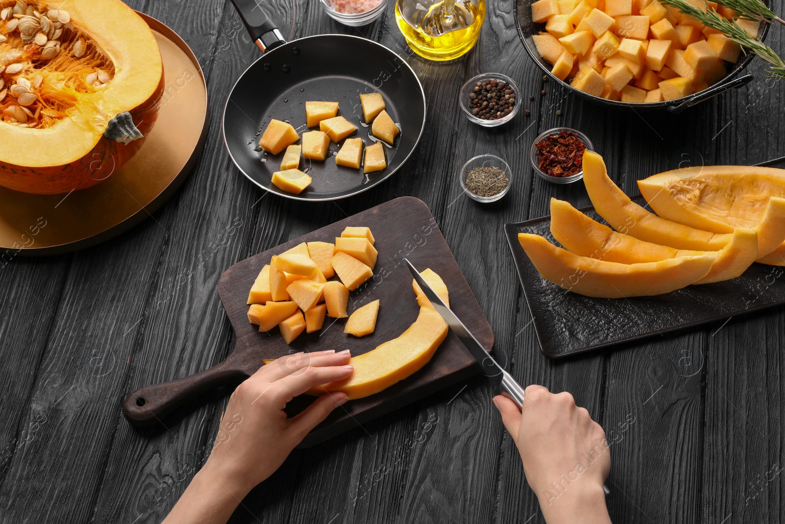 Photo of Woman cutting fresh pumpkin at black wooden table, above view