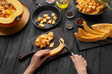 Woman cutting fresh pumpkin at black wooden table, above view