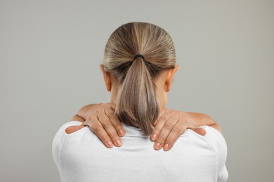 Photo of Mature woman suffering from pain in her neck on grey background, back view