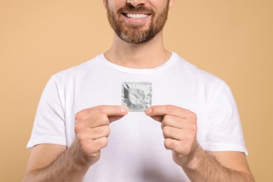 Man holding condom on beige background, closeup. Safe sex