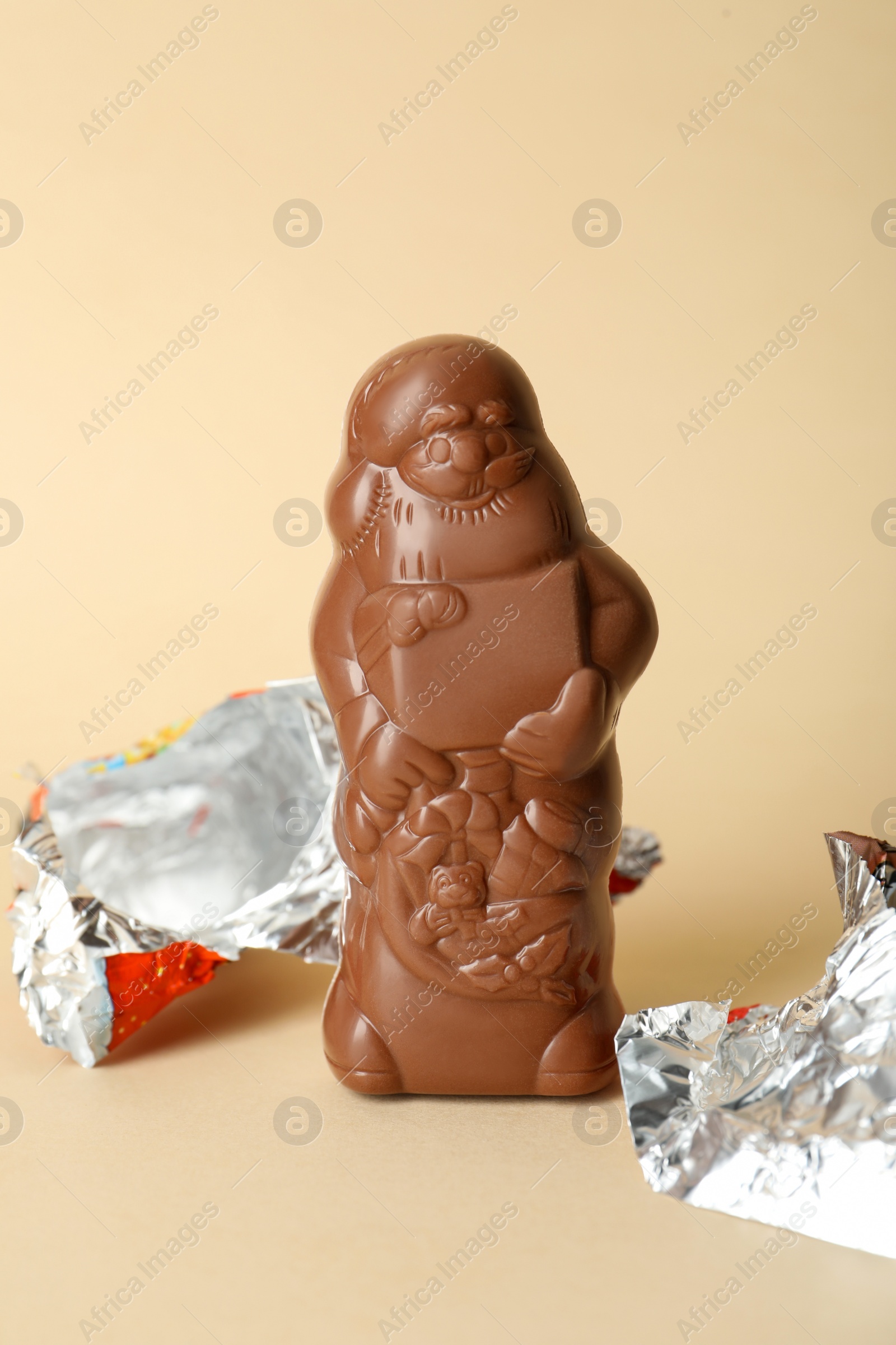 Photo of Unwrapped chocolate Santa Claus on beige background