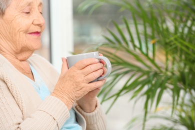 Photo of Elderly woman with cup of tea in nursing home, space for text. Assisting senior generation