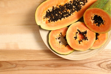 Photo of Plate with cut papayas on wooden table, top view. Space for text