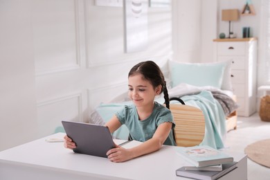 Little girl doing homework with tablet at table in bedroom