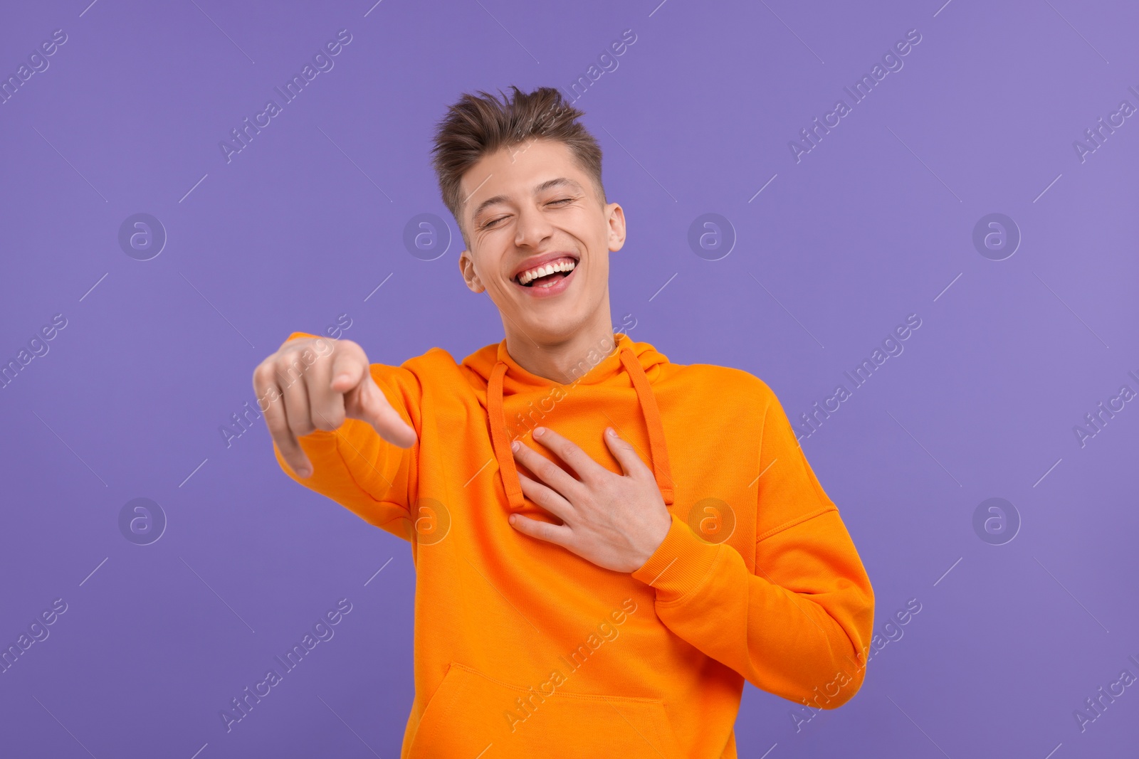 Photo of Young man pointing at something and laughing on violet background