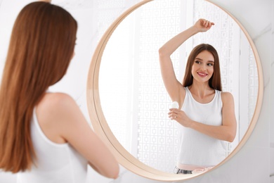 Beautiful young woman applying deodorant in bathroom