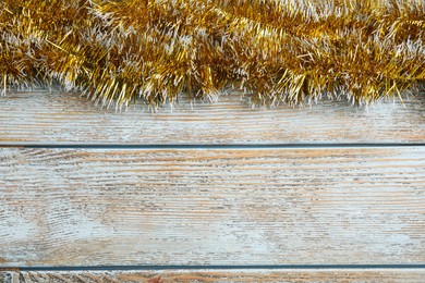 Golden tinsel on light blue wooden background, top view. Space for text