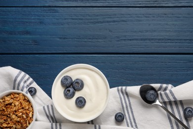 Photo of Bowl of tasty yogurt served with blueberries and muesli on blue wooden table, flat lay. Space for text