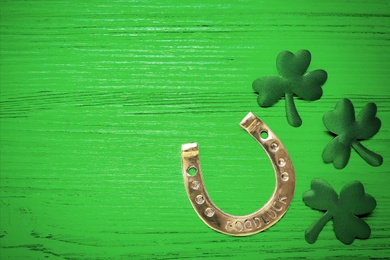 Image of Golden horseshoe and decorative clover leaves on green wooden table, flat lay with space for text. Saint Patrick's Day celebration