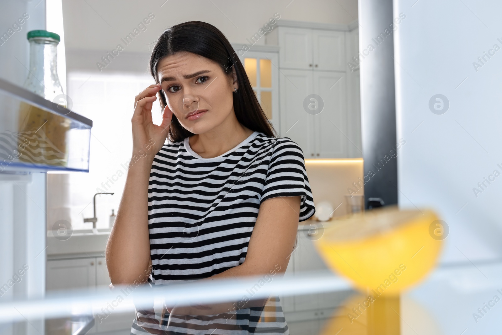 Photo of Upset woman near empty refrigerator in kitchen, view from inside