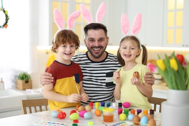 Painting Easter eggs. Happy father and his cute children with bunny ears at white marble table in kitchen