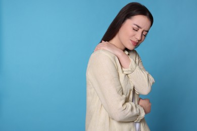 Photo of Young woman suffering from pain in shoulder on light blue background, space for text. Arthritis symptoms