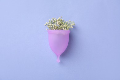 Menstrual cup with beautiful white flowers on blue background, top view