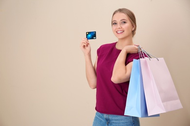 Portrait of happy young woman with credit card and shopping bags on color background, space for text. Spending money