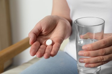 Woman with glass of water and pill on blurred background, closeup