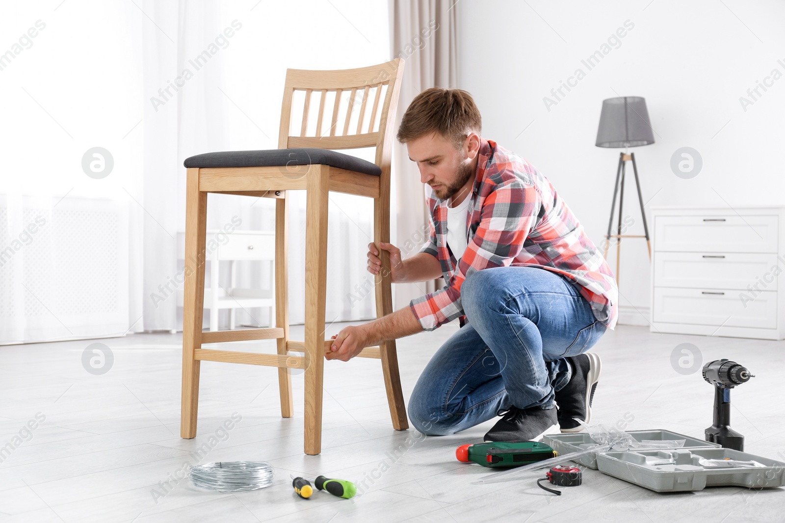 Photo of Young working man repairing chair at home