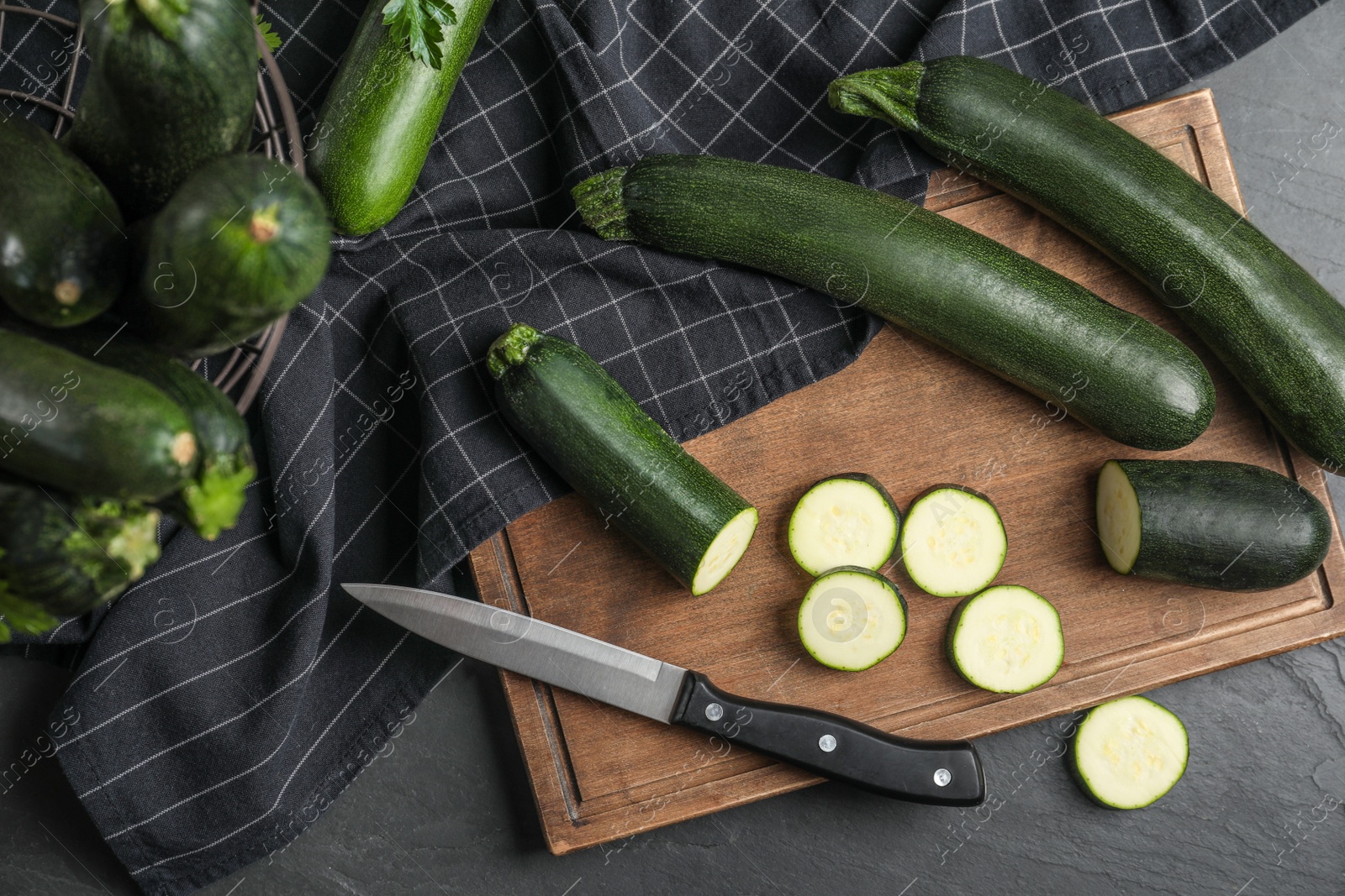 Photo of Green ripe zucchinis and wooden board on black slate table, flat lay