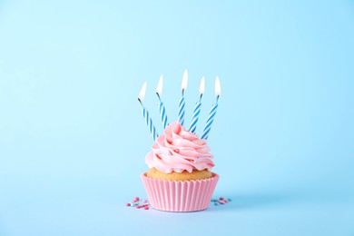 Photo of Delicious birthday cupcake with burning candles and sprinkles on light blue background