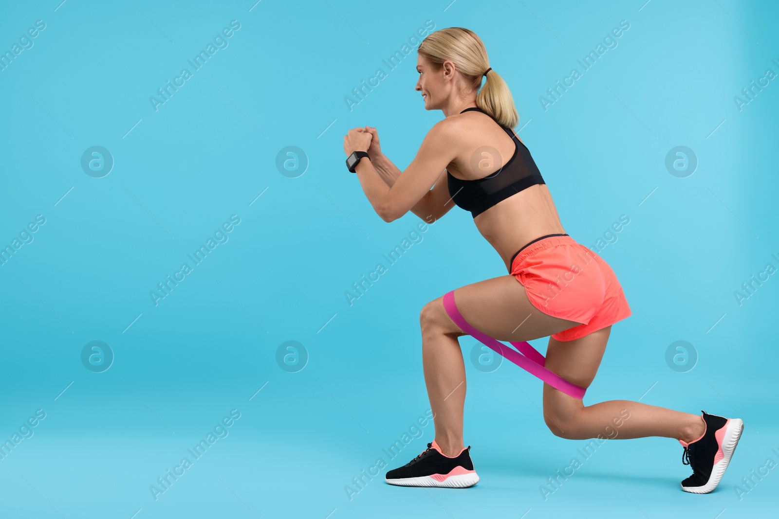 Photo of Woman exercising with elastic resistance band on light blue background. Space for text