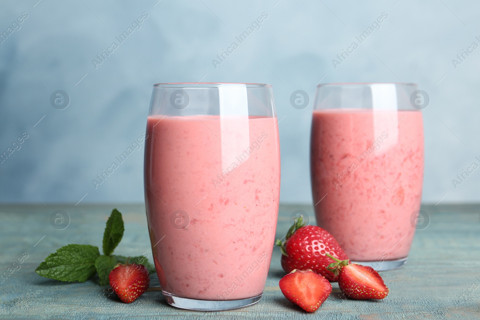 Photo of Tasty strawberry smoothies in glasses on blue wooden table