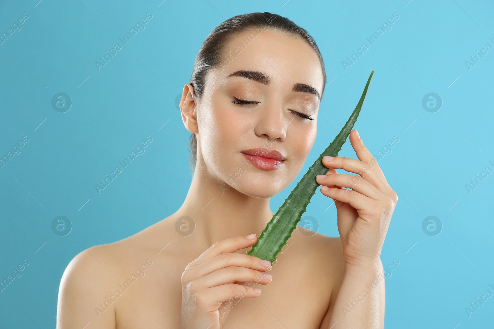 Photo of Young woman with aloe vera leaf on light blue background