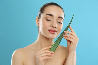 Photo of Young woman with aloe vera leaf on light blue background
