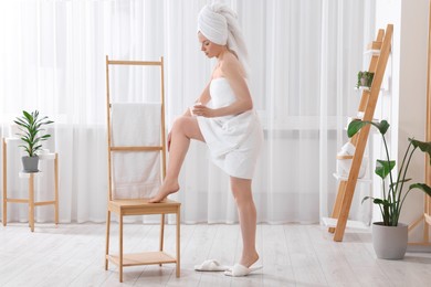 Photo of Beautiful young woman applying body cream onto leg indoors