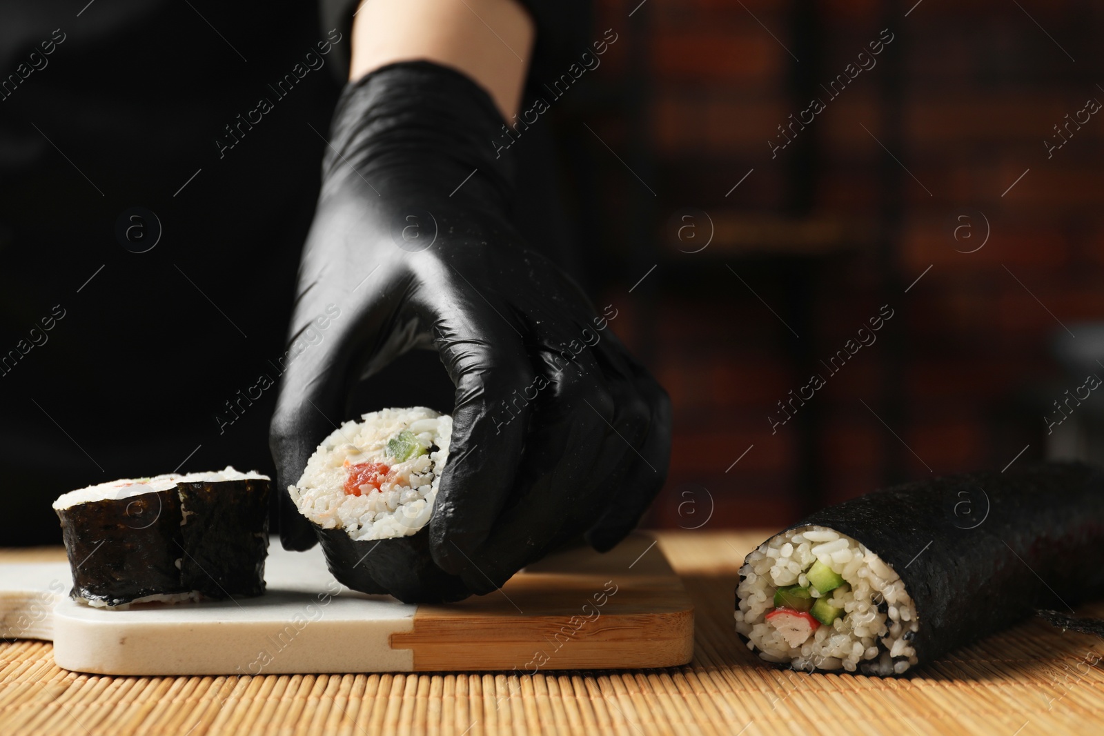 Photo of Chef in gloves putting sushi roll onto board at table, closeup