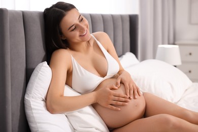 Beautiful pregnant woman in stylish comfortable underwear making heart with hands on her belly at home