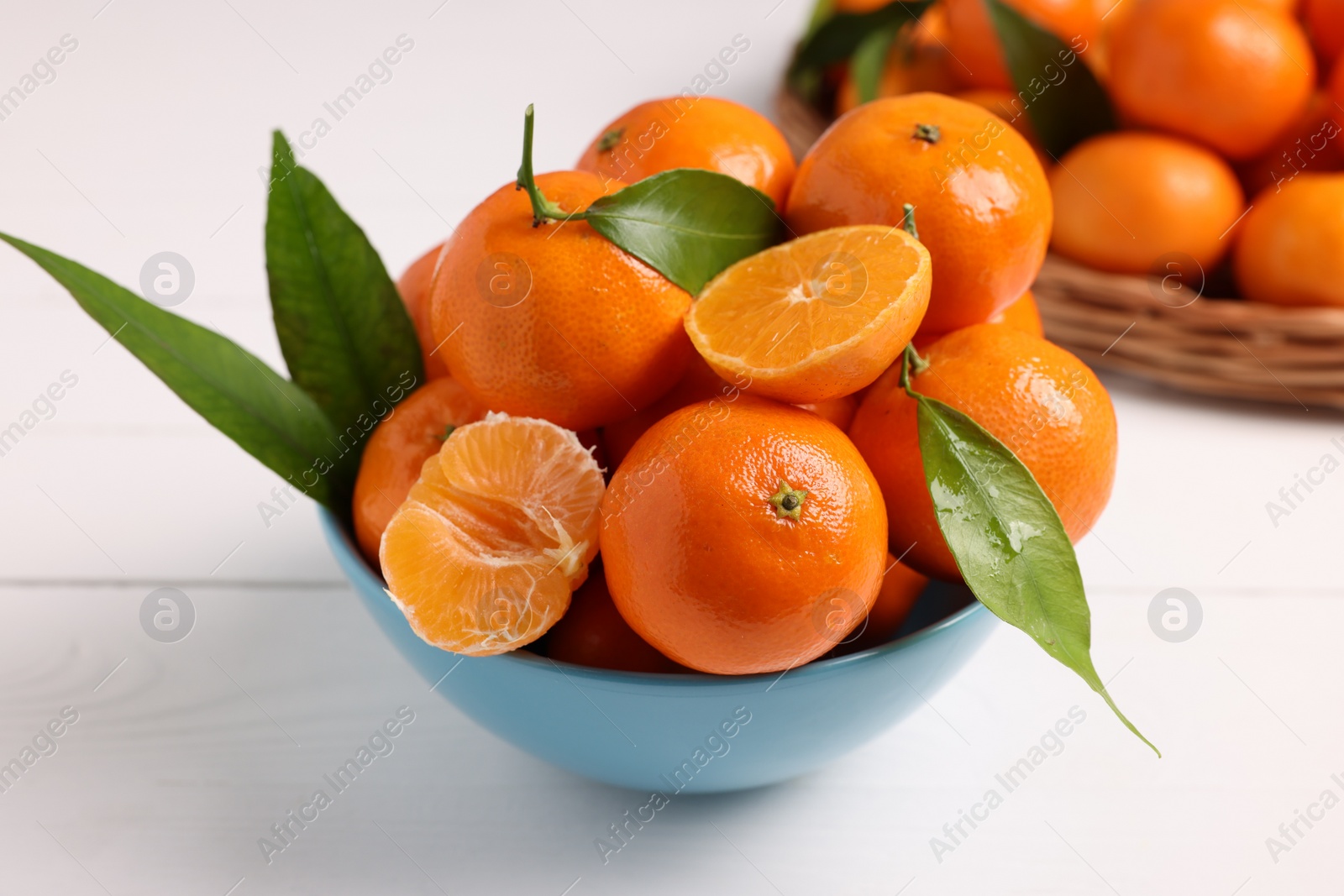 Photo of Fresh ripe juicy tangerines and green leaves in bowl on white wooden table, closeup