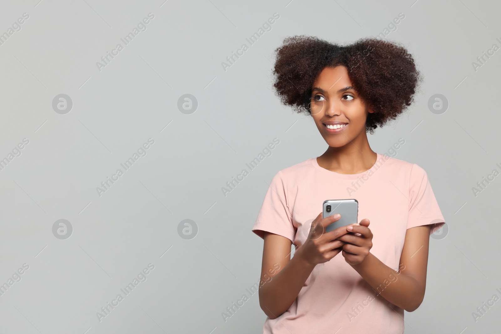 Photo of Smiling African American woman with smartphone on light grey background. Space for text