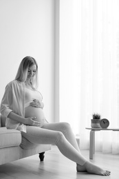 Photo of Beautiful pregnant woman sitting in light room at home, black and white effect