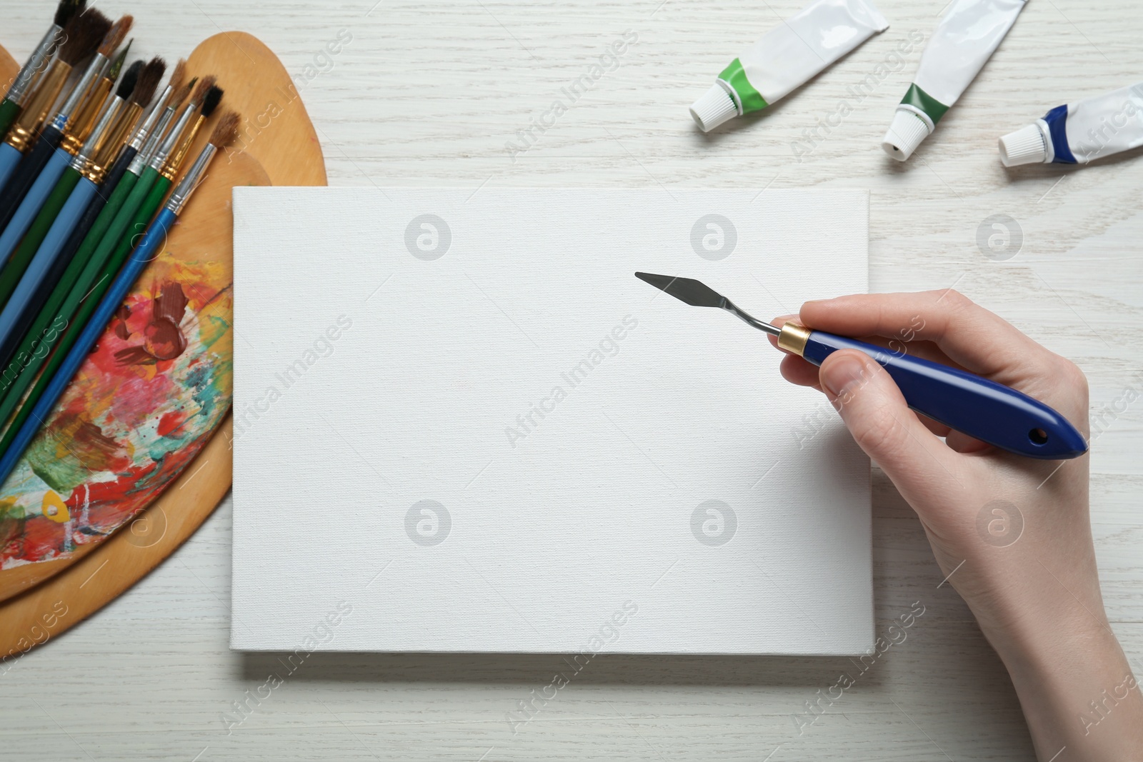 Photo of Man with spatula and blank canvas at white wooden table, top view