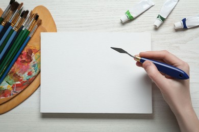 Photo of Man with spatula and blank canvas at white wooden table, top view