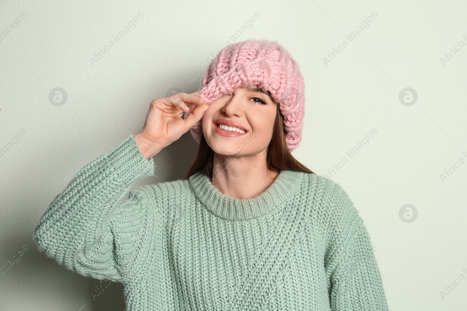 Photo of Young woman wearing warm sweater and hat on light background. Winter season