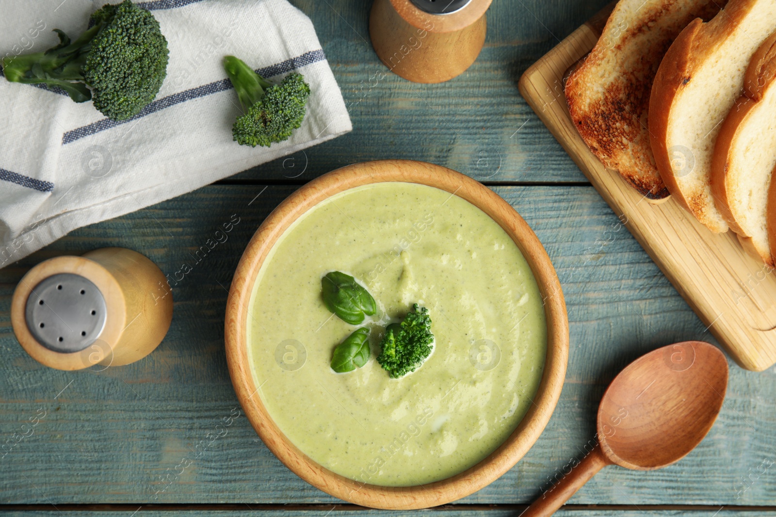 Photo of Delicious broccoli cream soup served on blue wooden table, flat lay