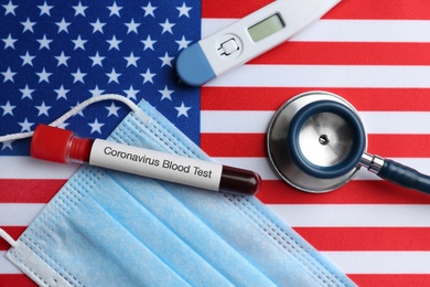 Photo of Test tube with blood sample, medical mask and stethoscope on American flag, flat lay. Coronavirus pandemic in USA