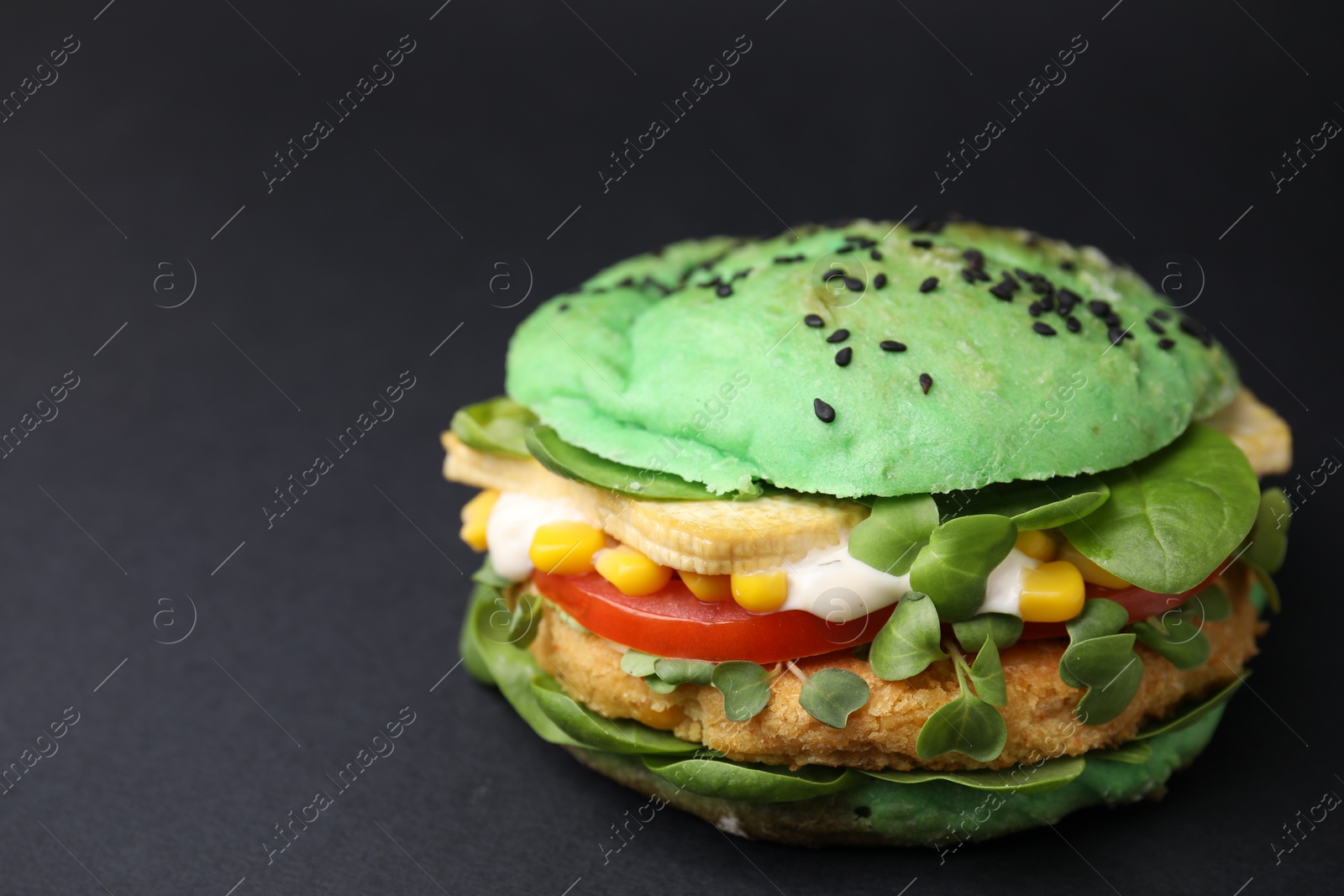 Photo of Tasty green vegan burger with vegetables, patty and microgreens on black background, closeup. Space for text