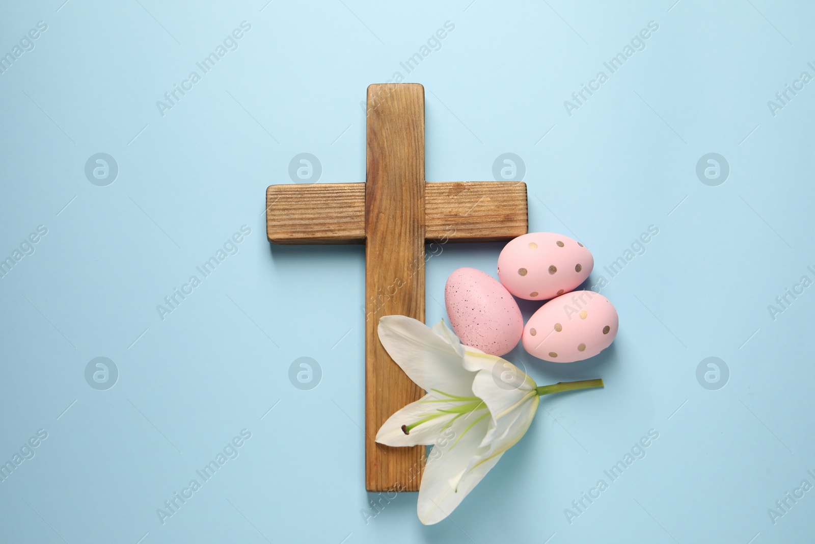Photo of Wooden cross, painted Easter eggs and lily flower on light blue background, top view