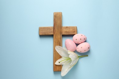 Wooden cross, painted Easter eggs and lily flower on light blue background, top view