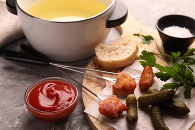 Fondue pot, forks with fried meat pieces, ketchup and other products on grey textured table