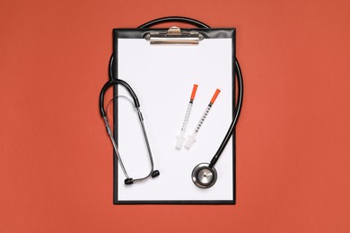 Stethoscope, syringes and clipboard on crimson background, top view. Medical tool