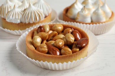 Photo of Different tartlets on white wooden table, closeup. Tasty dessert