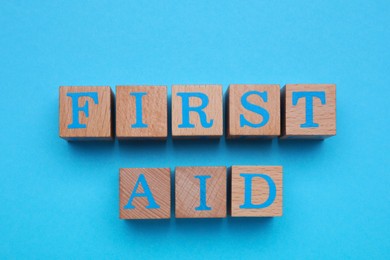 Words First Aid made of wooden cubes on light blue background, flat lay