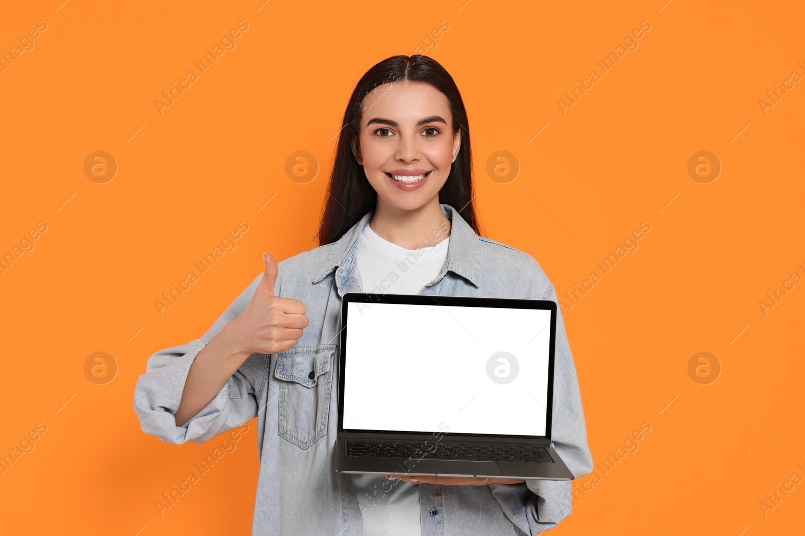 Photo of Happy woman with laptop showing thumb up on orange background