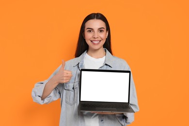 Photo of Happy woman with laptop showing thumb up on orange background