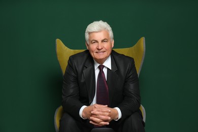 Happy mature businessman sitting in armchair against green background