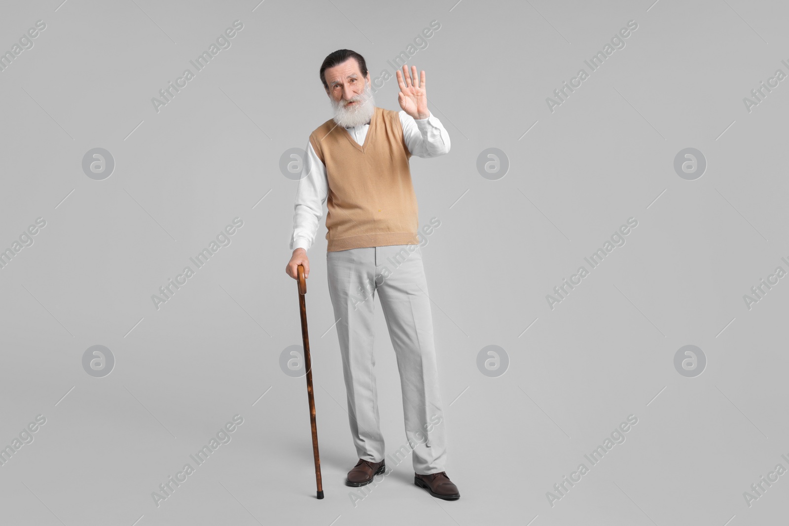 Photo of Senior man with walking cane waving on light gray background