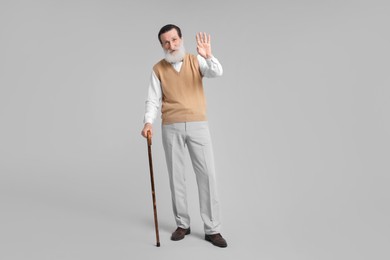 Photo of Senior man with walking cane waving on light gray background